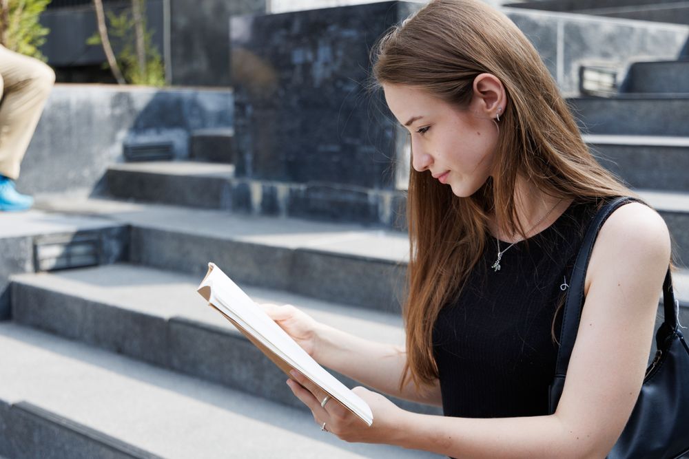 Woman reading book sitting on stairs in the city