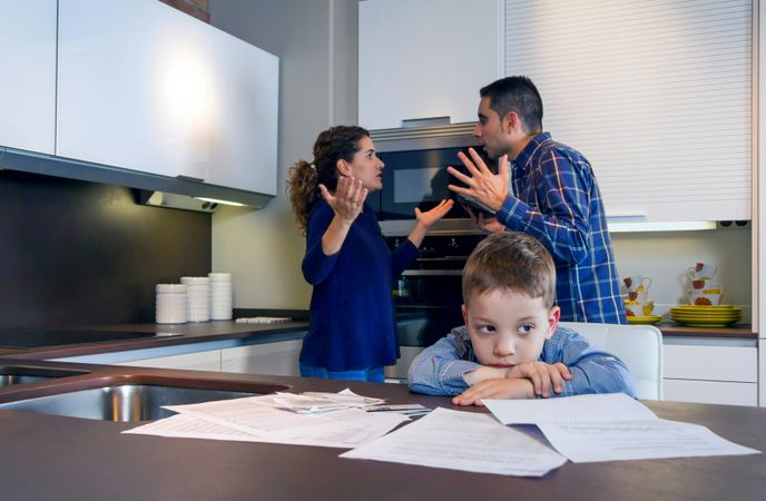 Couple arguing in front of son with bills strewn on the kitchen counter