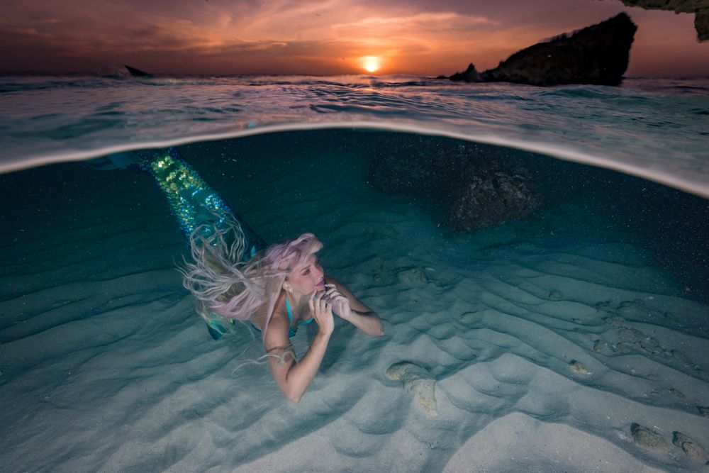 Blond fairytale female mermaid swimming along sea bottom