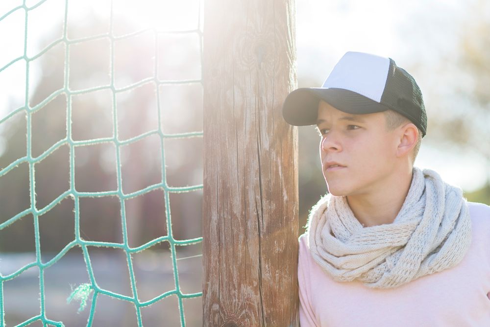 Portrait of a teenage male wearing a cap leaning on sports net