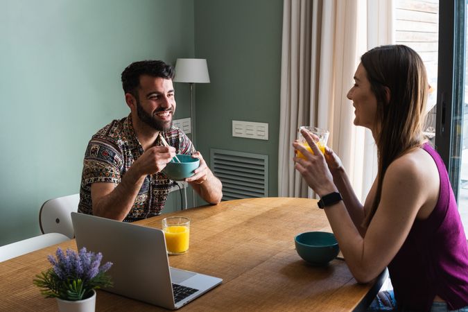 Happy friend having lunch and using laptop on dining table