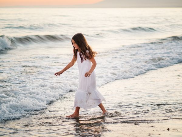 Adorable girl walking and playing on seaside at sunset