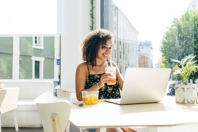 hispanic female with laptop enjoying healthy drink in cafe