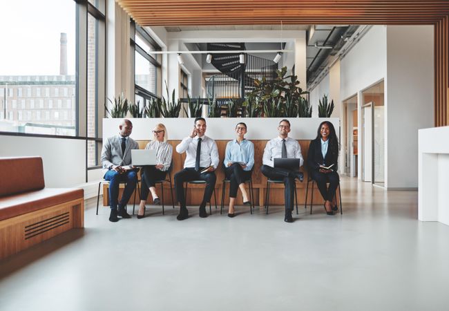 Group of people sitting and smiling in a row in a bright office