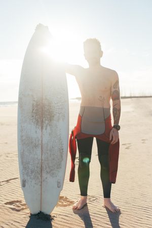 Portrait of surfer in the sun in wetsuit with surfboard, vertical