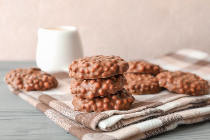 Stack of chocolate cookies on kitchen towel against light background, space for text