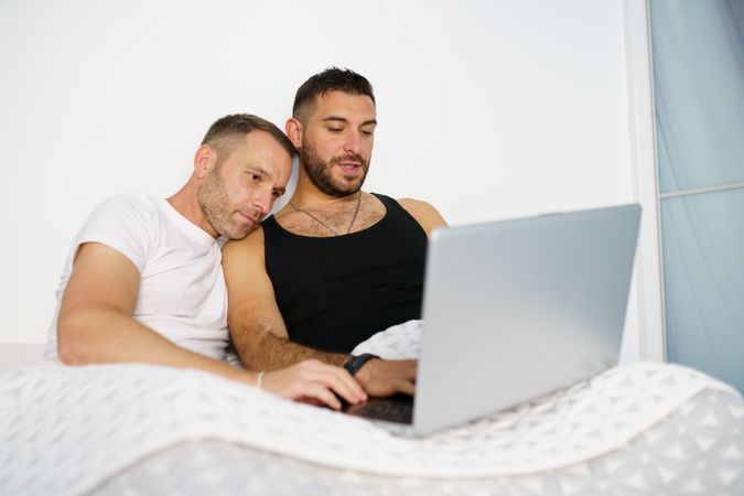 Male couple looking at laptop while relaxing in bed