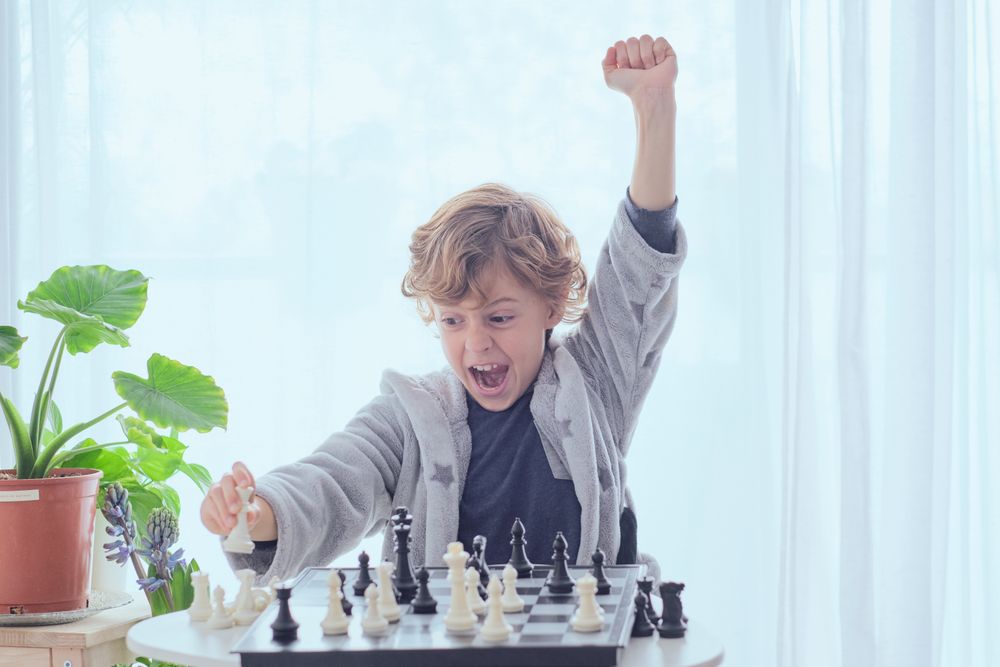 Cheerful preteen boy showing fist up gesture while winning chess