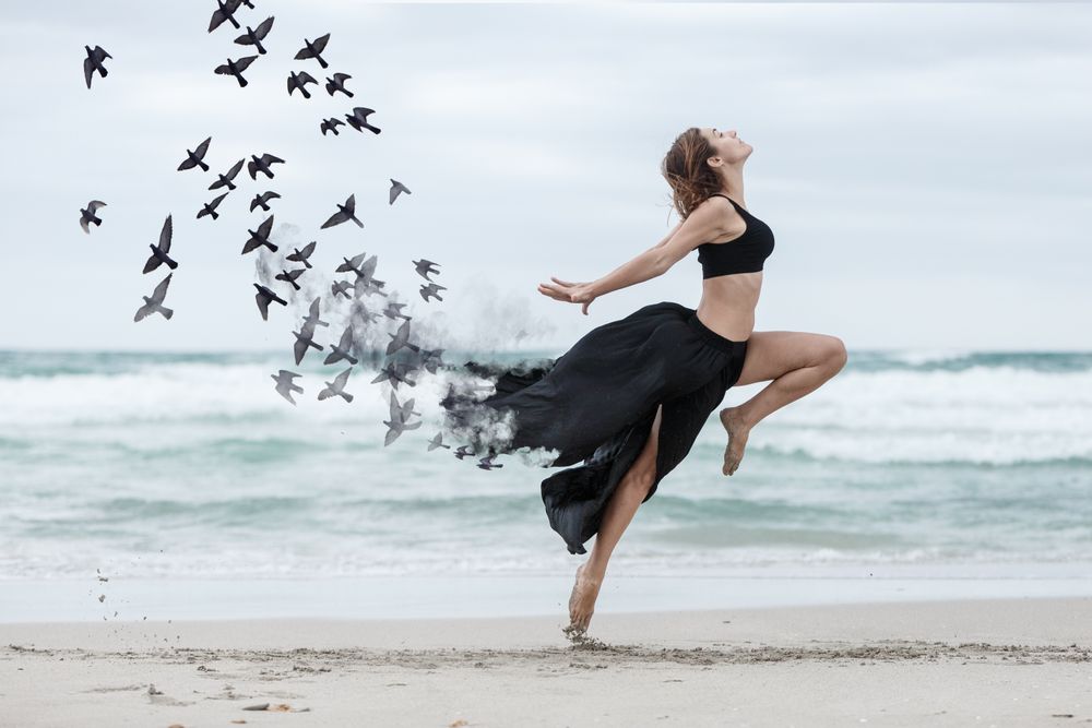 Young woman dancing with birds near sea