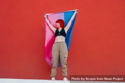 Young woman waving bisexual pride flag standing against red background 0vmepb