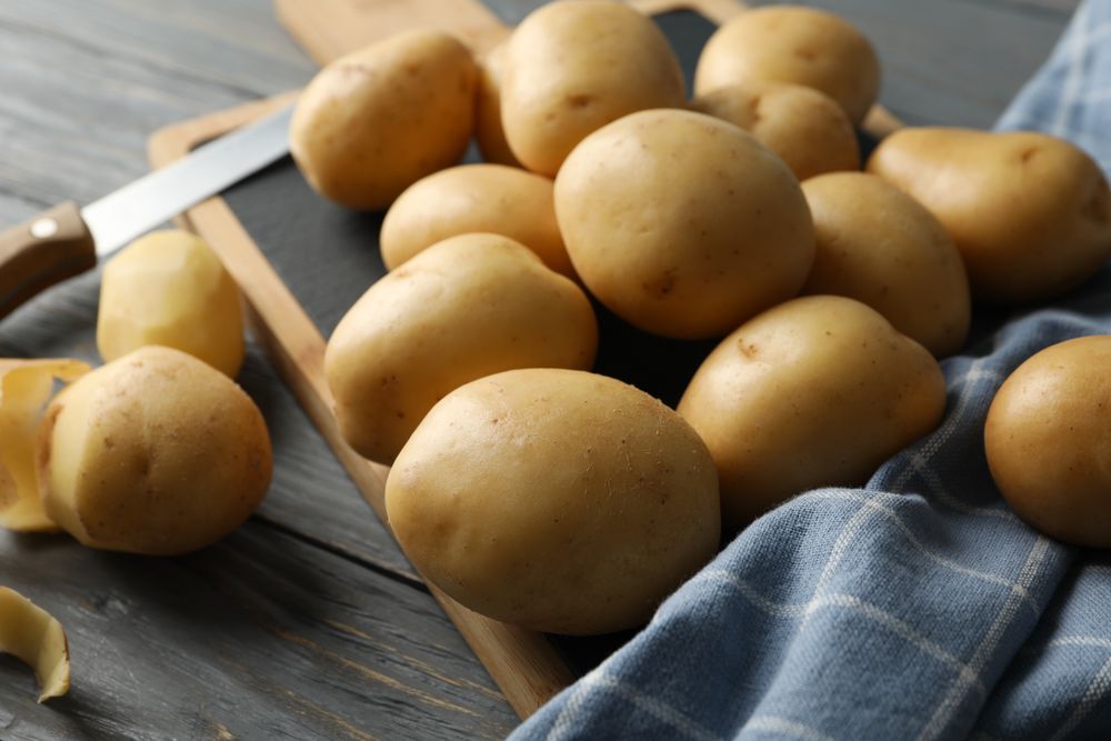 Breadboard with kitchen towel, knife and potatoes