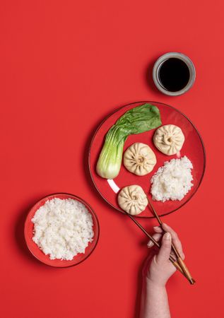 Person with chopstick eating chinese steamed food, top view on a red background