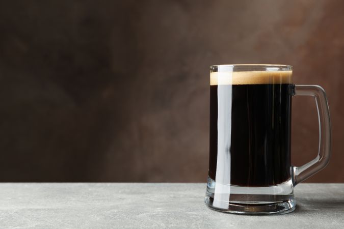 Glass of dark beer on grey table, space for text