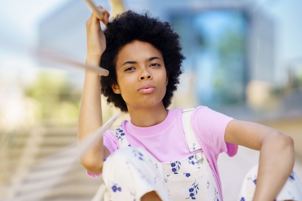 Woman in floral overalls sitting lost in thought leaning on handrail and looking in distance