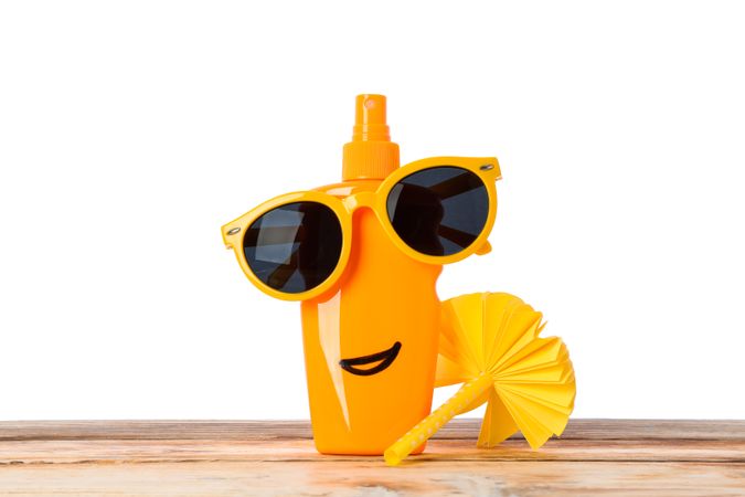 Sunscreen spray with sunglasses and decorative palm on wooden table, isolated on plain background. Safe tan