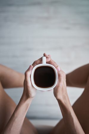 Crop woman sitting with coffee cup in hands at home