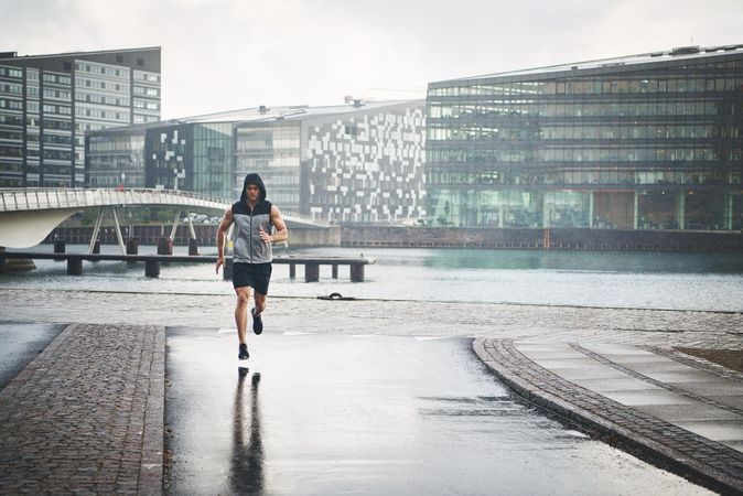 Muscular man in grey vest jogging outside on rainy day