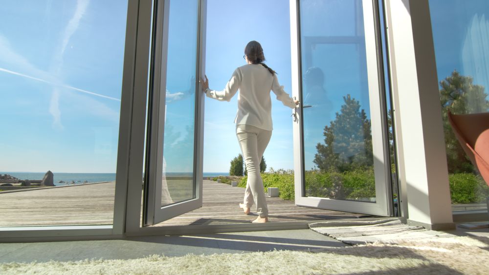 Shot of a Brunette with Loose Hair Opening Doors of the Balcony and Walking onto Sunny Terrace with Seaside View.