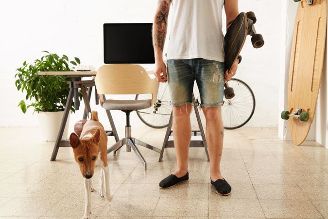 Tattoooed man in blank t-shirt holds surf skateboard in big loft