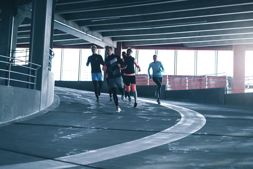 Group of people running down a sports track near bright window