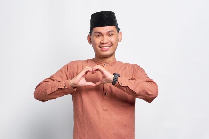 Smiling Muslim man in kufi head wear making heart shape with his hands