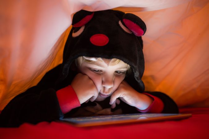Boy using tablet under blanket