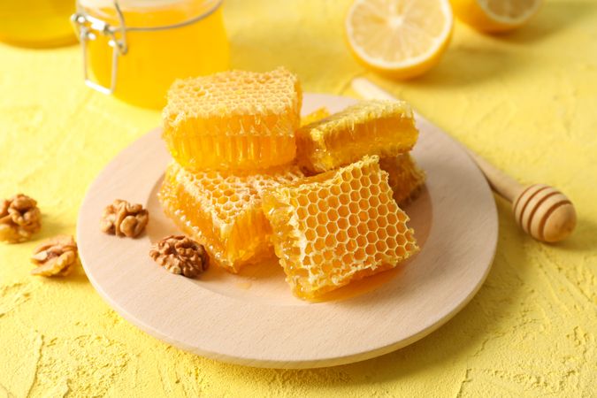 Walnut, honeycombs, jars with honey, dipper and lemon on yellow background, closeup