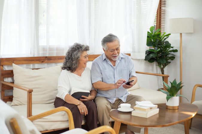 Happy Asian couple using smartphone together on couch in living room