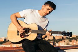 young man sitting playing acoustic guitar on a rooftop