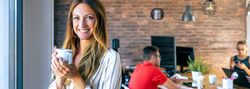 Happy businesswoman looking at camera drinking coffee in the off