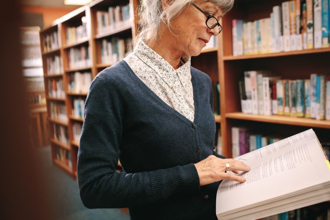Mature woman checking reference books at college campus library