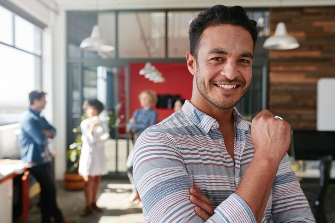 Happy biracial man standing in office with coworkers blurred in background