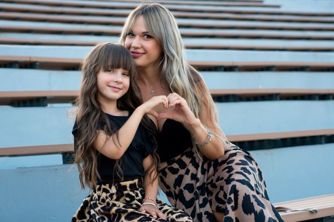 Mom and little daughter folded palms in shape heart