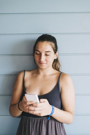 Content teenage female using cell phone while leaning against wood paneled wall