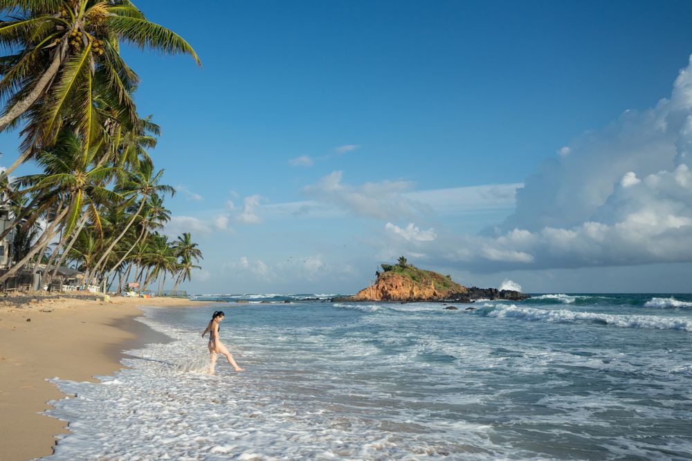 Young woman in water on sand beach with tropical forest