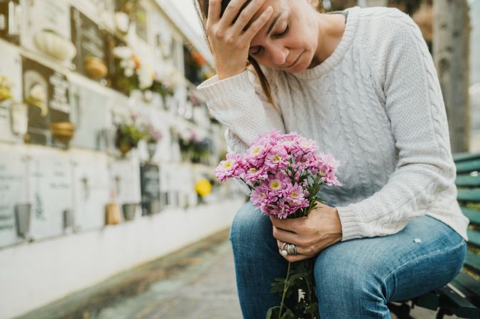 Crop mourning female touching forehead in cemetery
