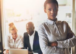 Black businesswoman pictured with her arms crossed in front of her colleagues
