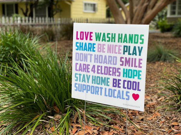 Angled view of yard sign with house behind reminding people to be kind