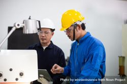 Asian man in blue jumpsuits and hard hats working with machinery 0W1164