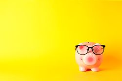 Happy piggy bank with glasses on yellow background, space for text. Finance, saving money