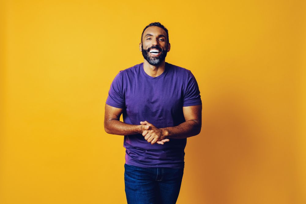 Black man smiling in yellow studio with hands together