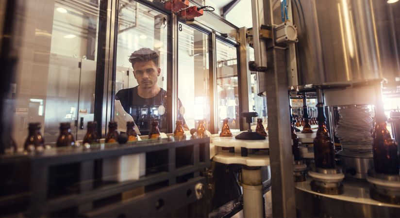 Factory worker looking at conveyor with beer beverage bottles moving
