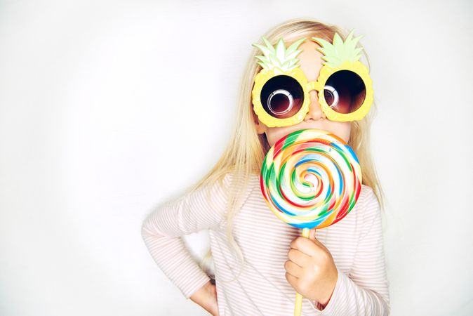 Blonde girl wearing big pineapple sunglasses with large lollypop