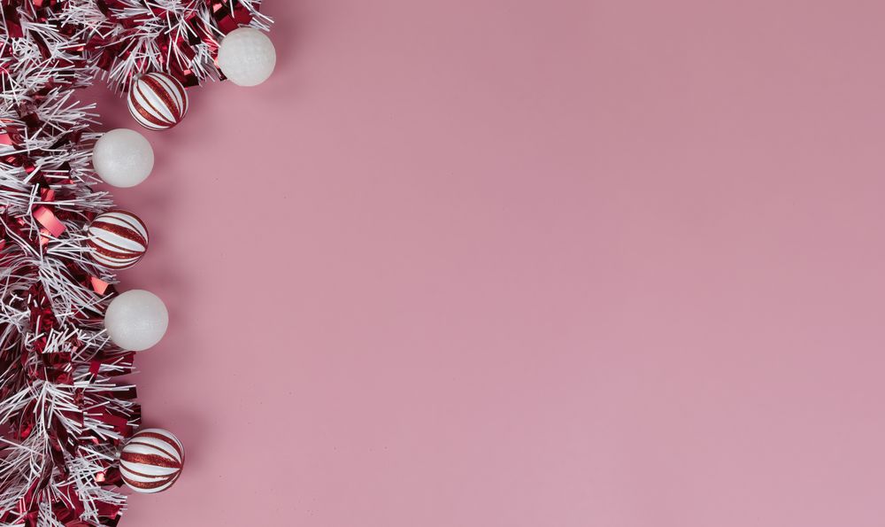 Top view of a red and tinsel plus ball ornaments on a light pink setting for a Merry Christmas or Happy New Year background