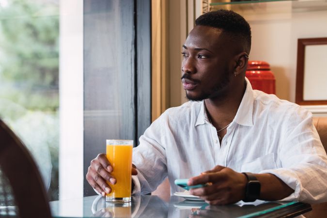 Serious Black man using smartphone in cafe while sipping an orange juice
