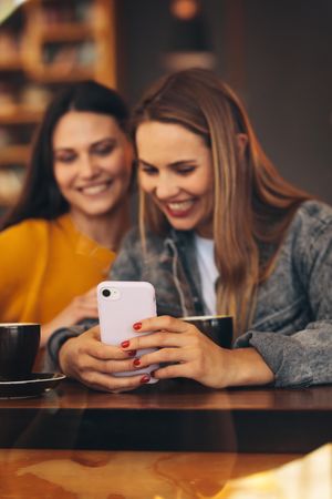 Women sitting together in a cafe looking at mobile phone and smiling