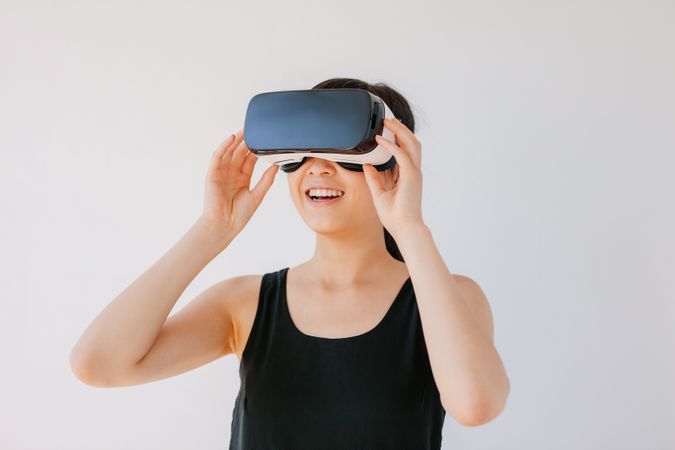 Happy young woman in VR headset looking away at the objects in virtual reality