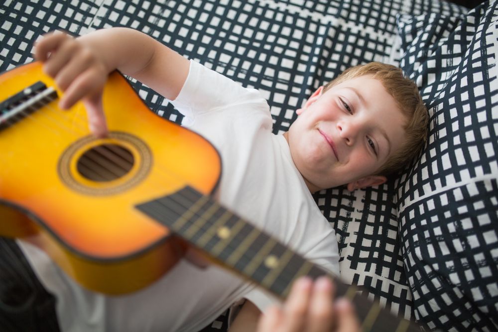 Young blonde boy playing toy guitar
