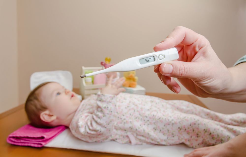 Hands holding thermometer before cute baby