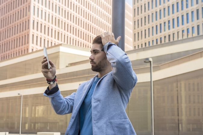 Man in blazer checking phone with hand on hair